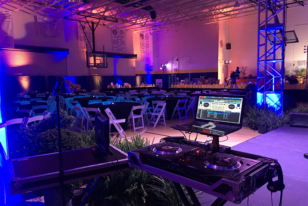 DJ controller and uplighting set up for an event in a large hall with blue and pink lighting