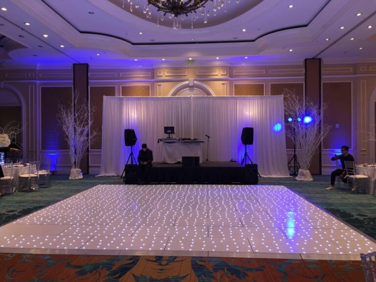 Hotel ballroom with an LED dance floor, white draping and blue uplighting around the DJ booth