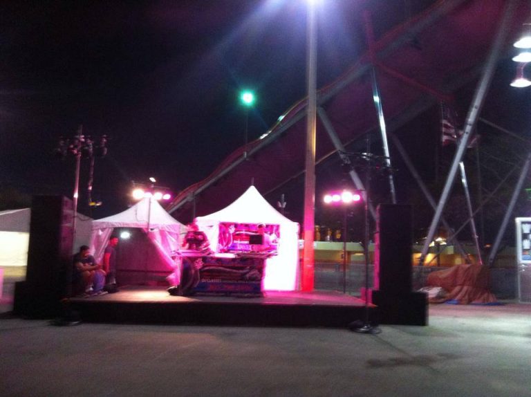 Outdoor night event with DJ tent, pink lighting and stage truss